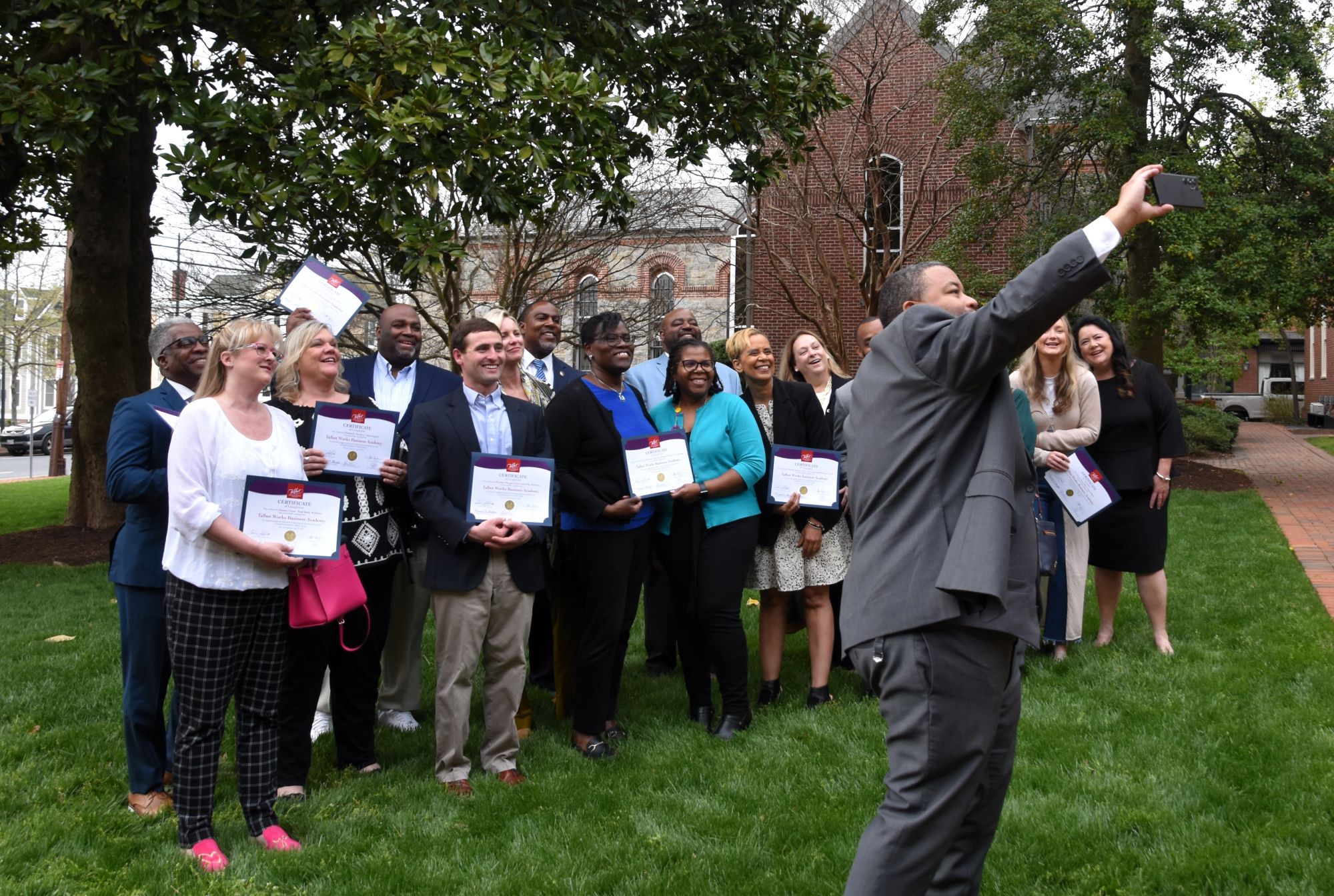 The Talbot Works Business Academy’s inaugural graduates gather on the courthouse lawn to celebrate their graduation, with program facilitator Will Holmes taking a selfie.